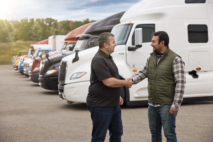 A person shaking hands with another person in front of trucks