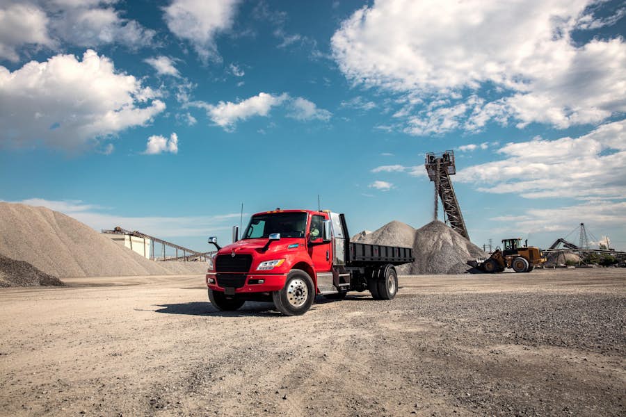 A red truck in a dirt area with piles of gravel and machinery